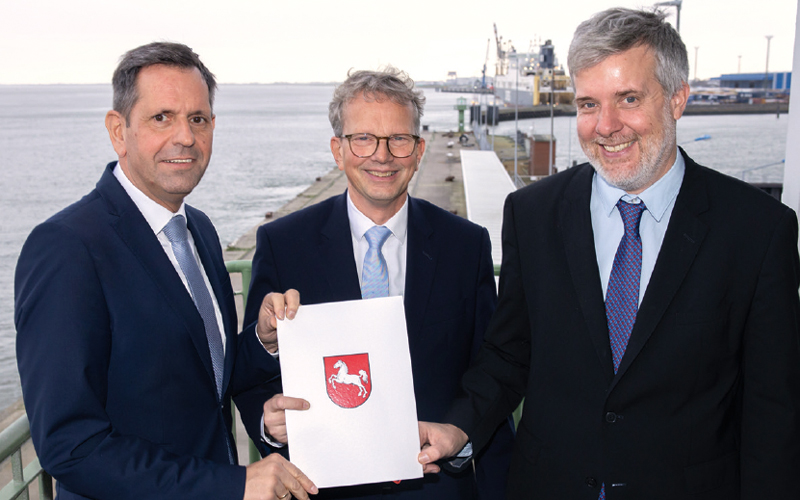 Group photo with Olaf Lies, Holger Banik and Dieter Janecek, the former holding a document with the Lower Saxony coat of arms up to the camera